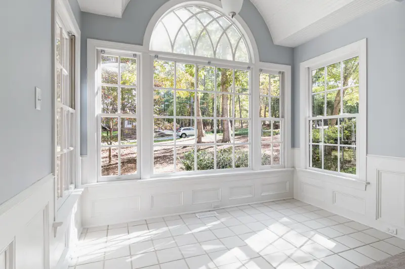 A bright sunroom with tall arched windows onto trees